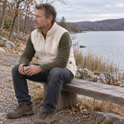 Man wearing the cream fleece vest while resting beside a lake