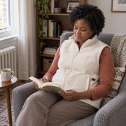 Woman reading at home in the ThermStride cream heated fleece vest